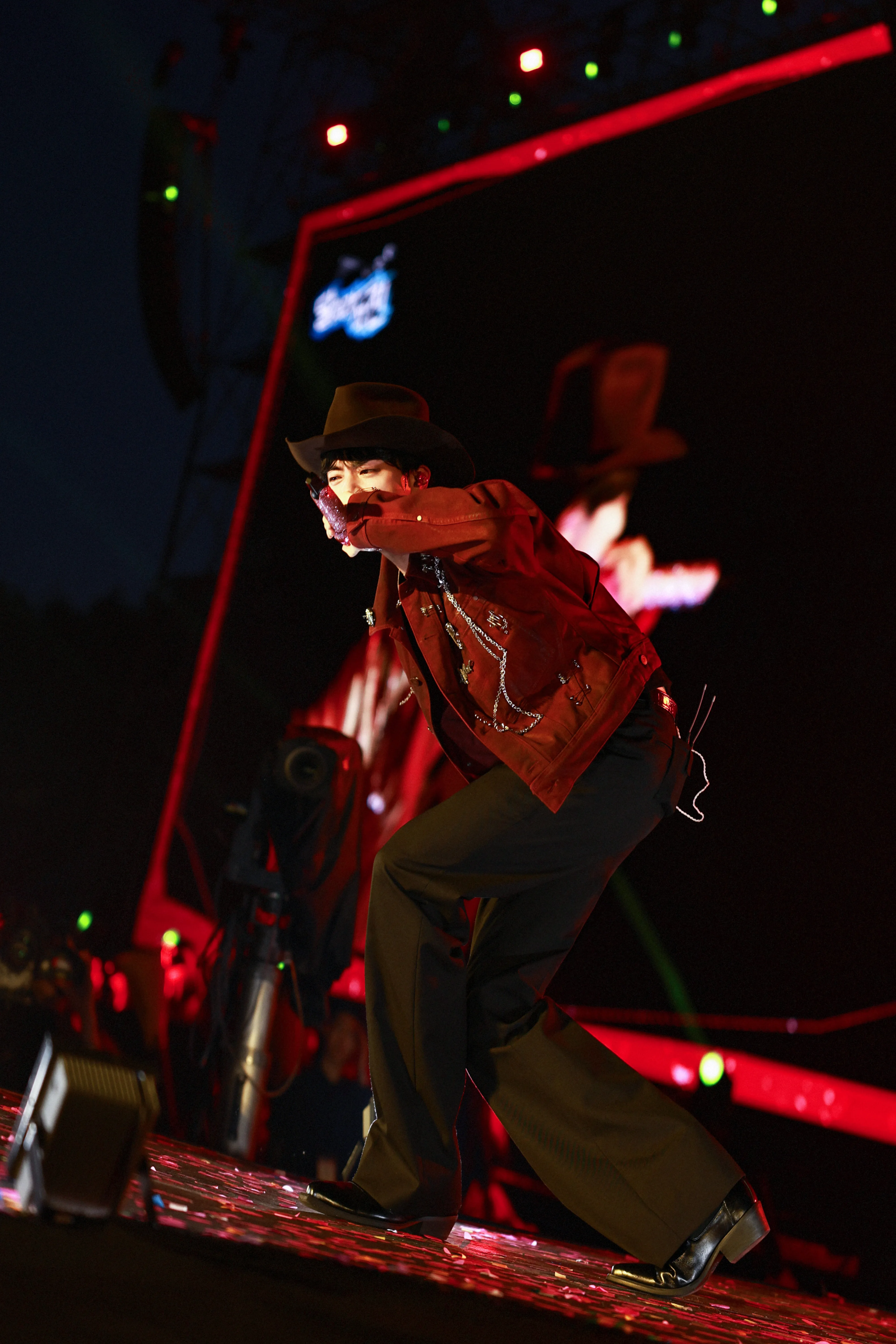 BTS' Kim Seok Jin singing on stage, wearing cowboy hat with red LED lighting background