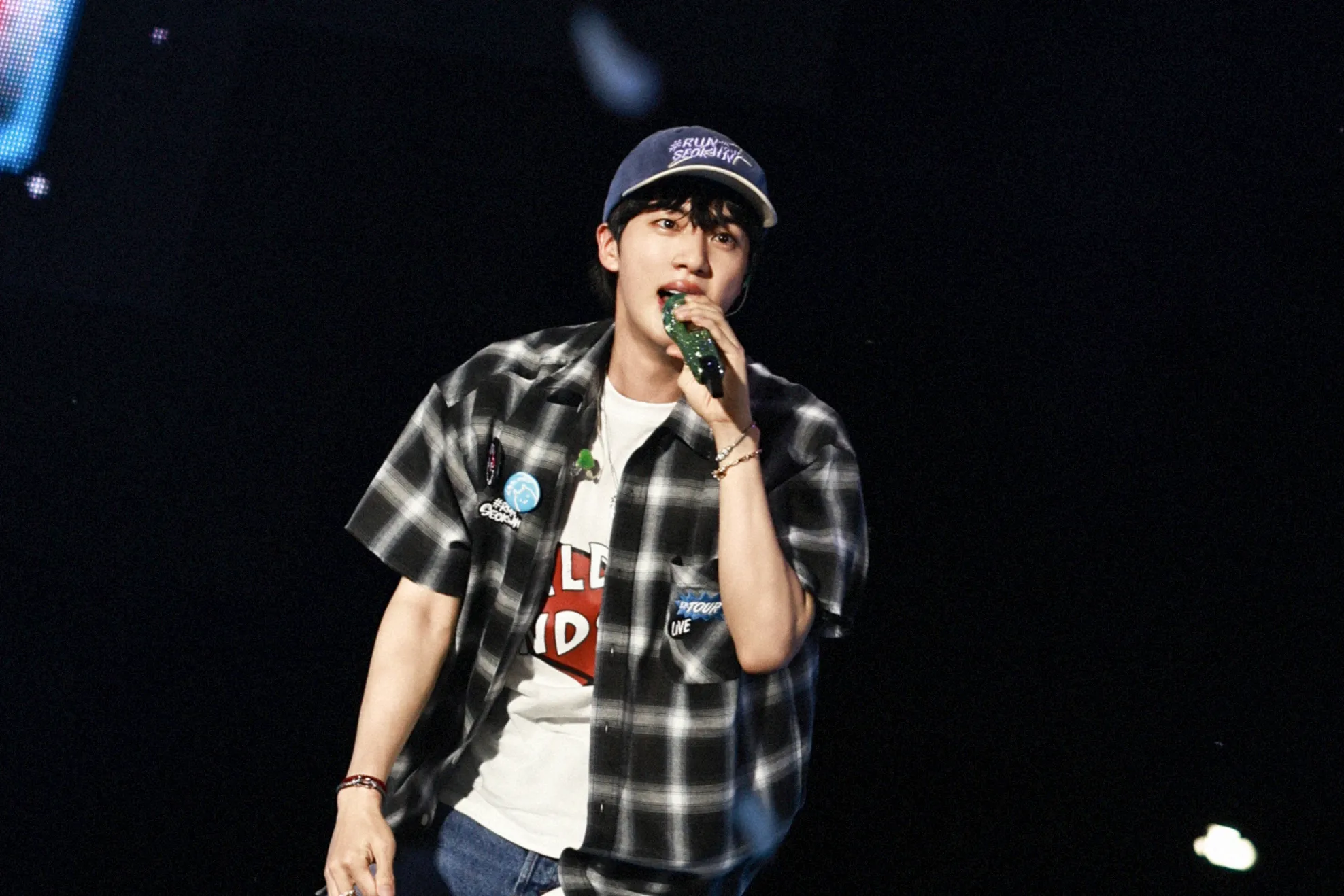 BTS' Kim Seok Jin singing on stage, with casual wear and cap
