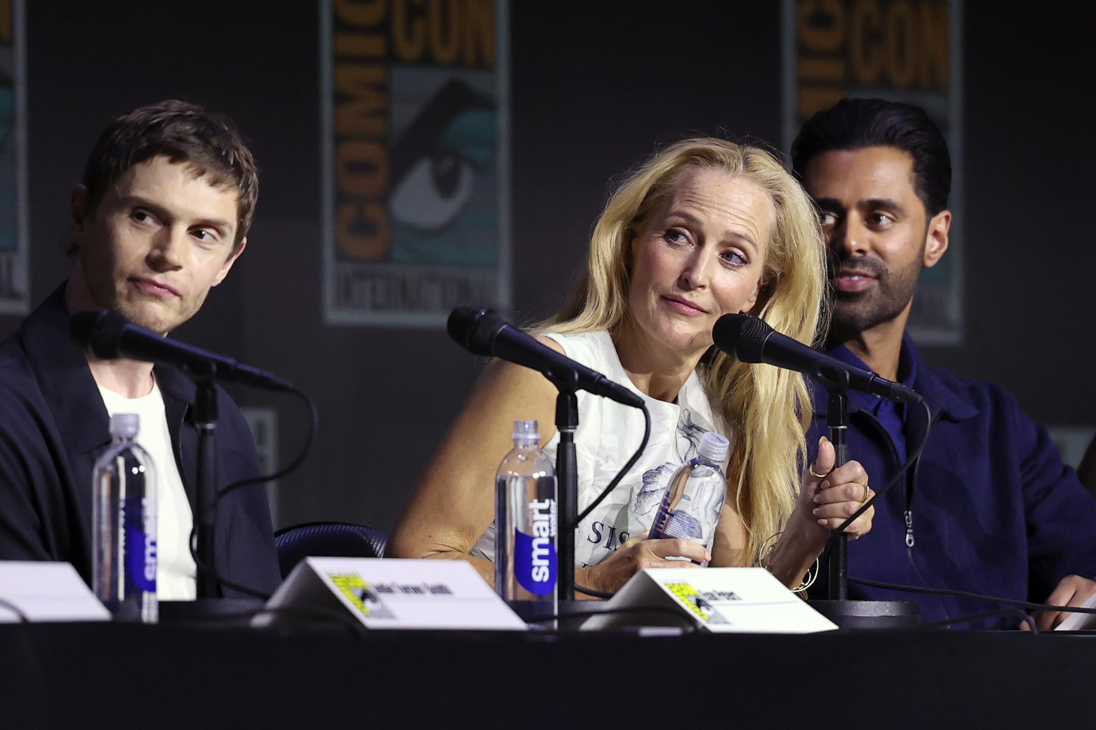 Evan Peters, Gillian Anderson, and Hasan Minhaj speaking on the Tron: Ares Comic-Con panel, discussing the upcoming film with fans and press.